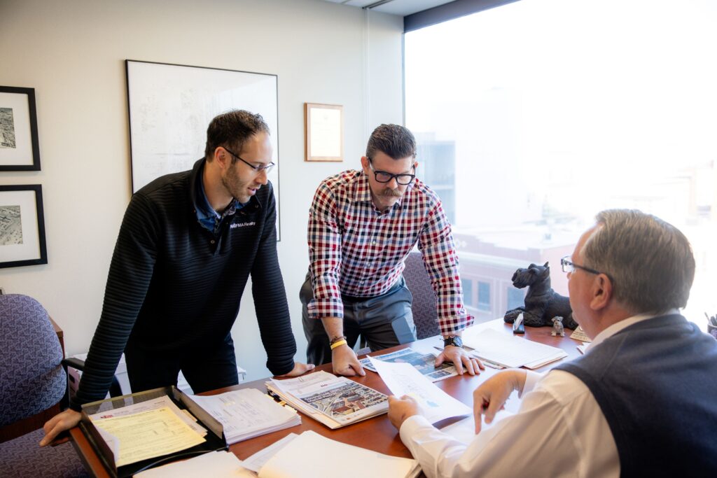 Three NAI FMA Realty associates reviewing documents together at a desk in a bright office.