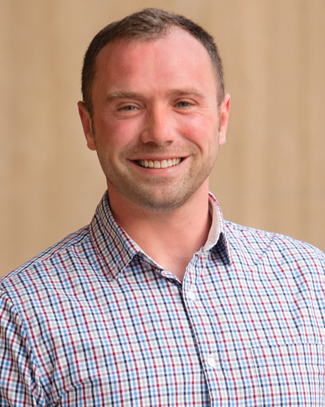 Portrait of Joel McGill, Project Coordinator at NAI FMA Realty, standing in an office setting.
